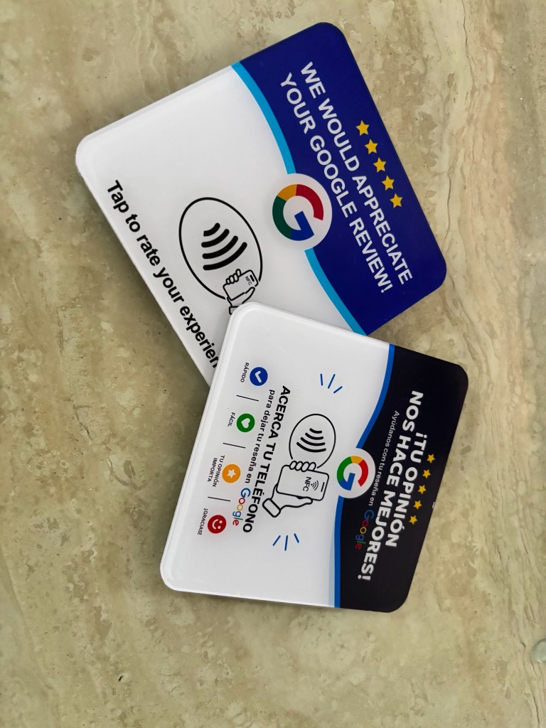 Las dos tarjetas NFC de Google Reviews (inglés y español) sobre superficie de mármol