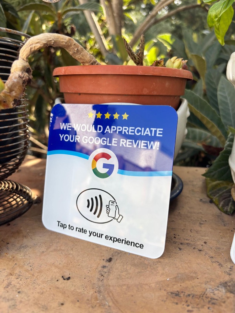 Tarjeta NFC Google Reviews en inglés apoyada en maceta de barro con planta en patio