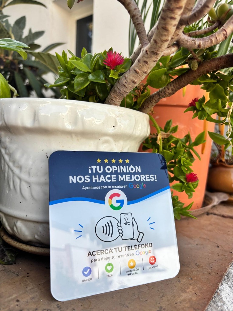 Tarjeta NFC Google Reseñas en español apoyada en maceta blanca con flores rojas en patio andaluz