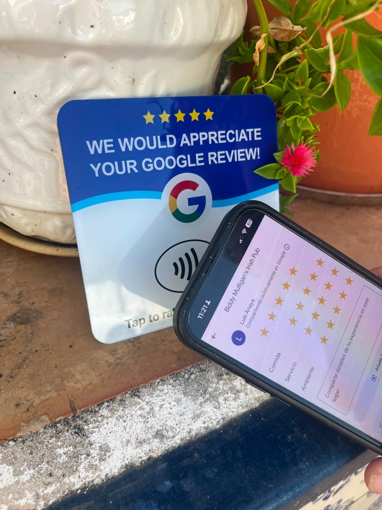 Tarjeta NFC junto al móvil mostrando la pantalla de Google con 5 estrellas seleccionadas en el patio